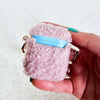 A woman holds up a plush pink AirPod Case Cover with a golden-colored keychain accent by Fleece Chic.