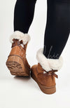 A pair of winter boots that're brown and fur-lined with a back bow are worn by a person in black leggings - Fleece Chic