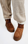 A person wears a pair of winter boots that're brown with a pair of Light Taupe knit pants by Fleece Chic.