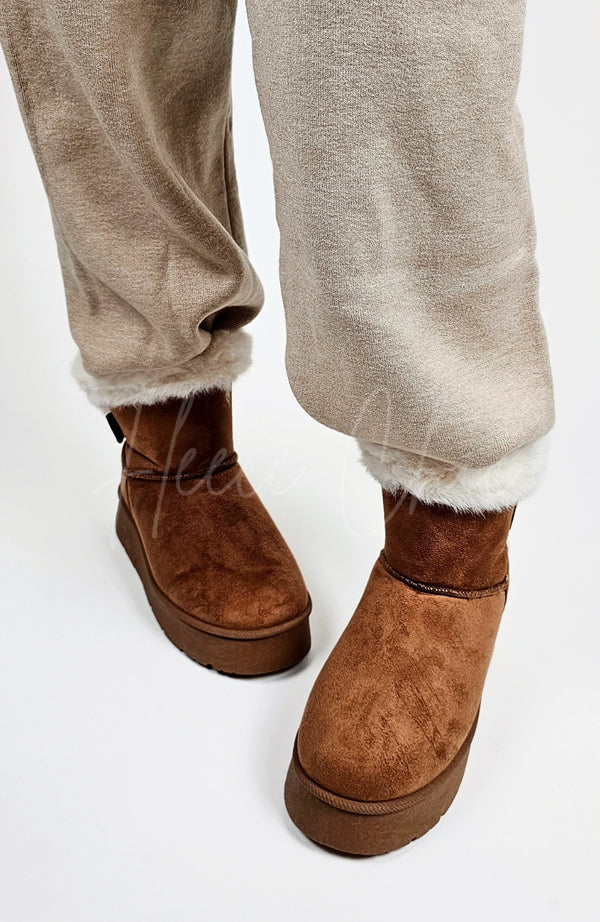 A person wears a pair of winter boots that're brown with a pair of Light Taupe knit pants by Fleece Chic.