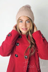 A woman wears a pink fleece beanie with a cute pom pom on it by Fleece Chic paired with a red coat.