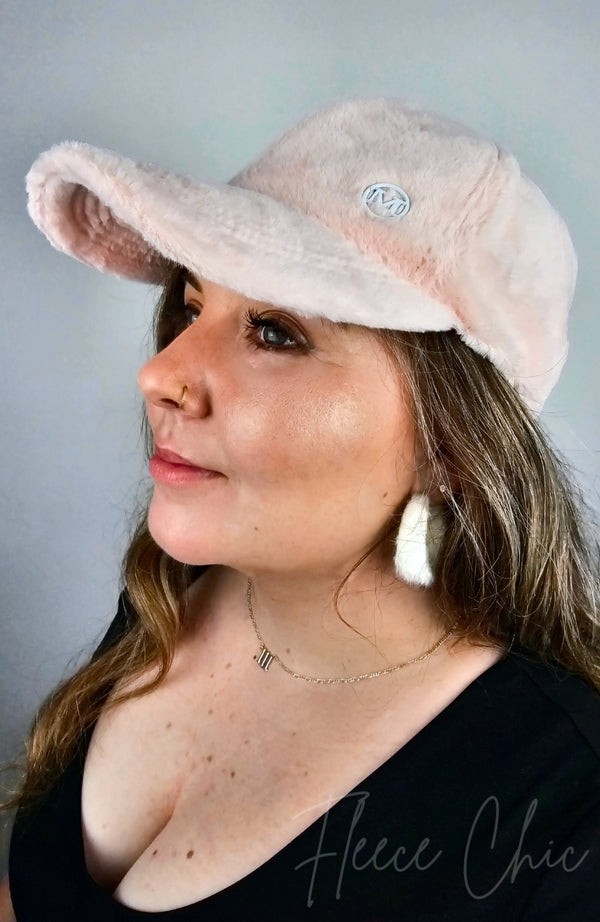 A woman in a black shirt poses in a pink Fur Baseball Cap and medium hoop earrings by Fleece Chic.