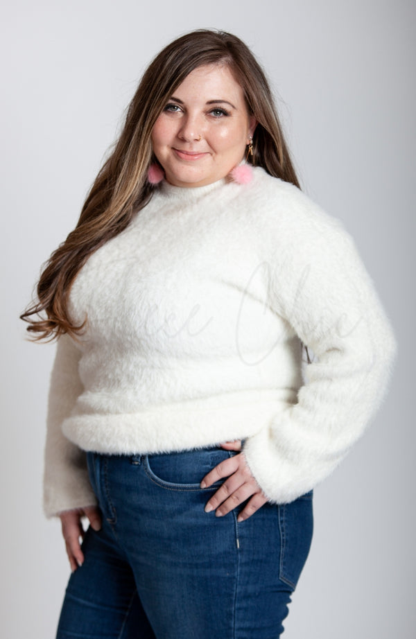 A woman poses in a soft sweater that is white with pink long drop earrings by Fleece Chic.