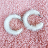 Medium hoop earrings that are white and fluffy have a close up on a fuzzy pink background - Fleece Chic
