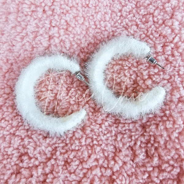 Medium hoop earrings that are white and fluffy have a close up on a fuzzy pink background - Fleece Chic