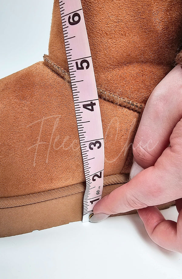 A close-up detail shot of a pair of winter boots by Fleece Chic showing their heel height compared to a measuring tape.