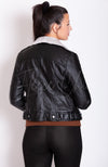 A woman faces away from the camera turned to the side while wearing a black Vegan Leather Jacket by Fleece Chic.