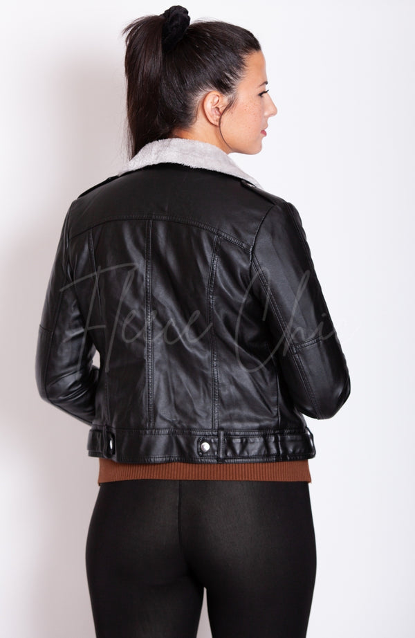 A woman faces away from the camera turned to the side while wearing a black Vegan Leather Jacket by Fleece Chic.