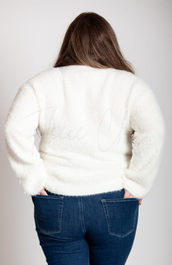 A woman stands with her hands in her jean pockets while modeling the backside of a fuzzy soft sweater by Fleece Chic.