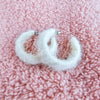 Medium hoop earrings that are white and fluffy are displayed in a close up on a fuzzy pink background - Fleece Chic