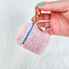 A woman dangles a plush pink AirPod Case Cover with a golden-colored keychain accent, showing its backside - Fleece Chic