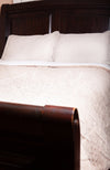 A sherpa comforter by Fleece Chic is shown on a made bed with dark wooden furnishing.