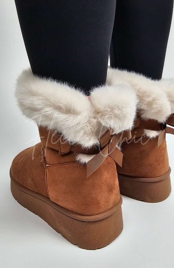 A pair of winter boots that're brown and fur-lined with a back bow are worn by a person in black leggings - Fleece Chic