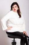 A woman sits on a stool while wearing a white soft sweater, thermal leather leggings, and plush hoop earrings by Fleece Chic.