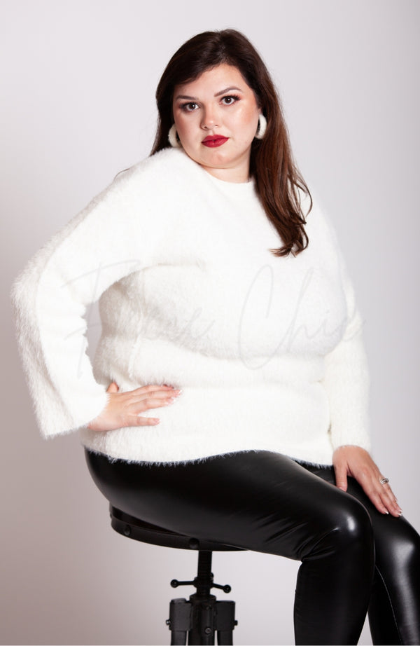 A woman sits on a stool while wearing a white soft sweater, thermal leather leggings, and plush hoop earrings by Fleece Chic.