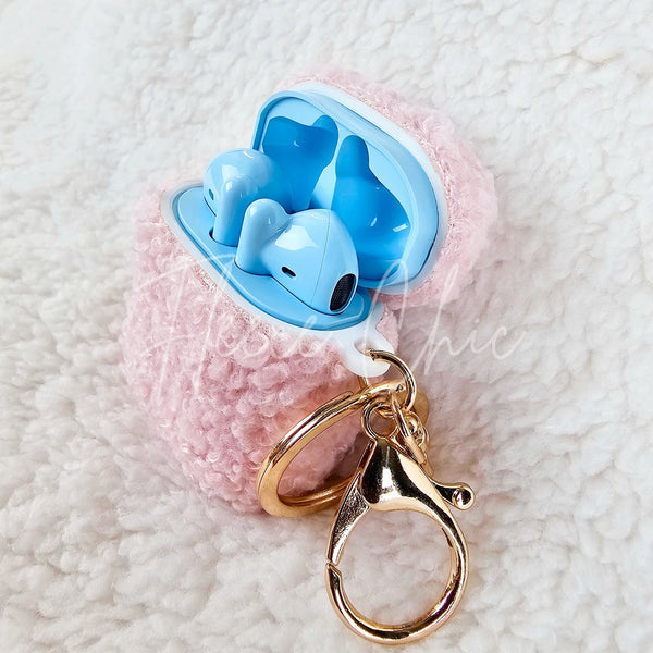 A teddy AirPod Case Cover that is light pink with a golden-colored keychain accent by Fleece Chic withlight blue earbuds inside.