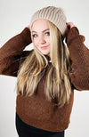A woman with blonde hair wears Fleece Chic's beige Fleece Beanie paired with a brown sweater.