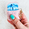 A plush pink AirPod Case Cover with a golden-colored keychain accent, held between fingers - Fleece Chic