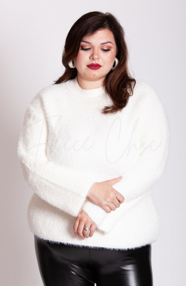 A woman wears a soft sweater that is white, thermal leather leggings, and plush hoop earrings by Fleece Chic.