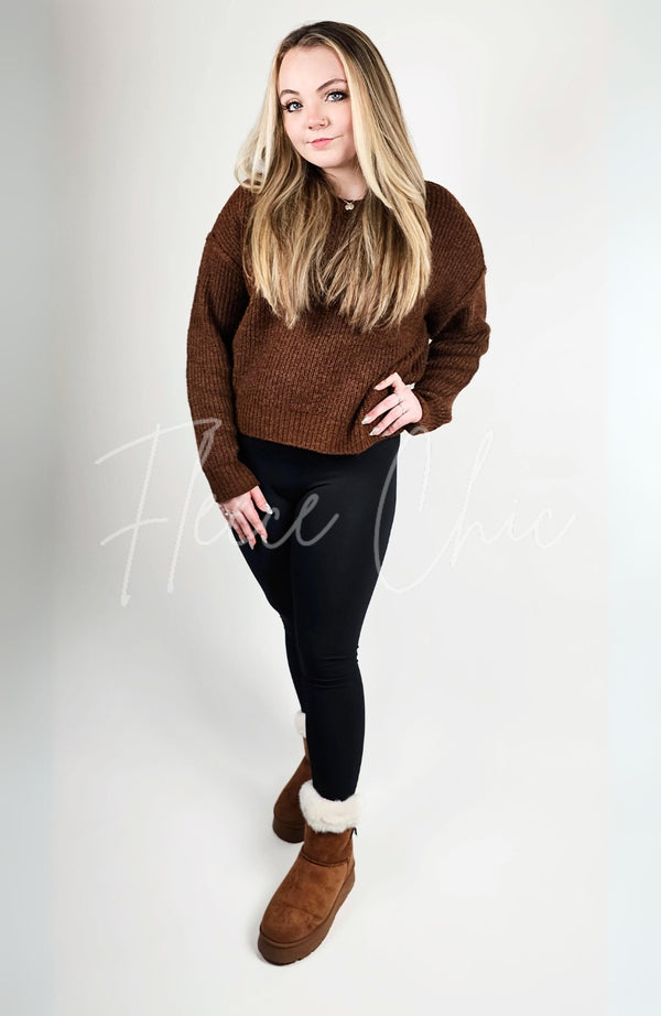 A woman with blonde hair poses in a pair of winter boots, black leggings, and a brown sweater - Fleece Chic