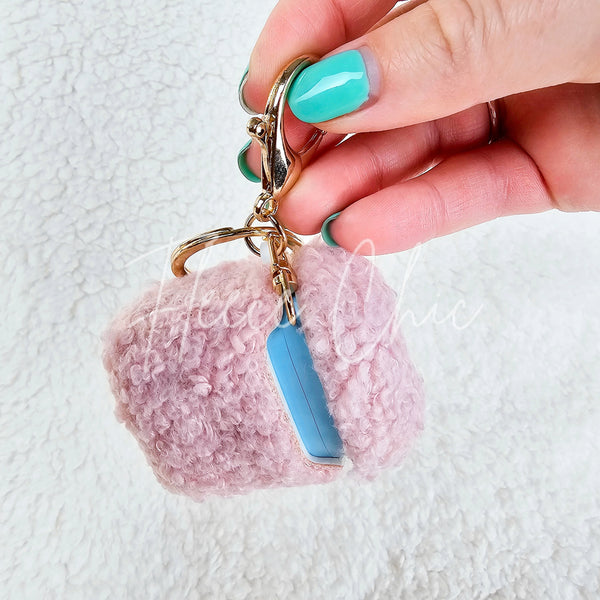 A woman dangles a plush pink AirPod Case Cover with a golden-colored keychain accent, showing its front side - Fleece Chic