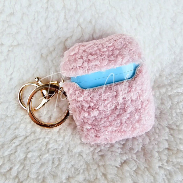 A teddy AirPod Case Cover that is light pink with a golden-colored keychain accent by Fleece Chic on a sherpa background.