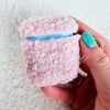 A woman holds up a plush pink AirPod Case Cover with a golden-colored keychain accent, showing its front side - Fleece Chic