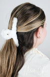A claw hair clip that is made of white plush is used to pull back a woman's brown hair - Fleece Chic