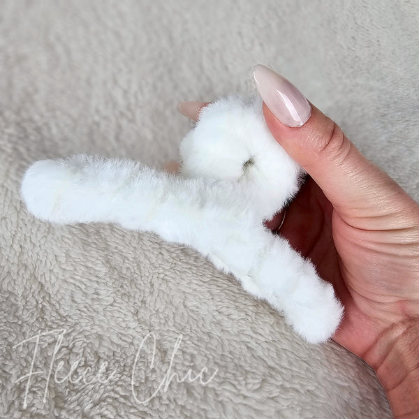 A person holds a white fluffy claw hair clip by Fleece Chic.