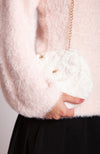 A woman wearing a pink fuzzy sweater holds a white fur purse by Fleece Chic.