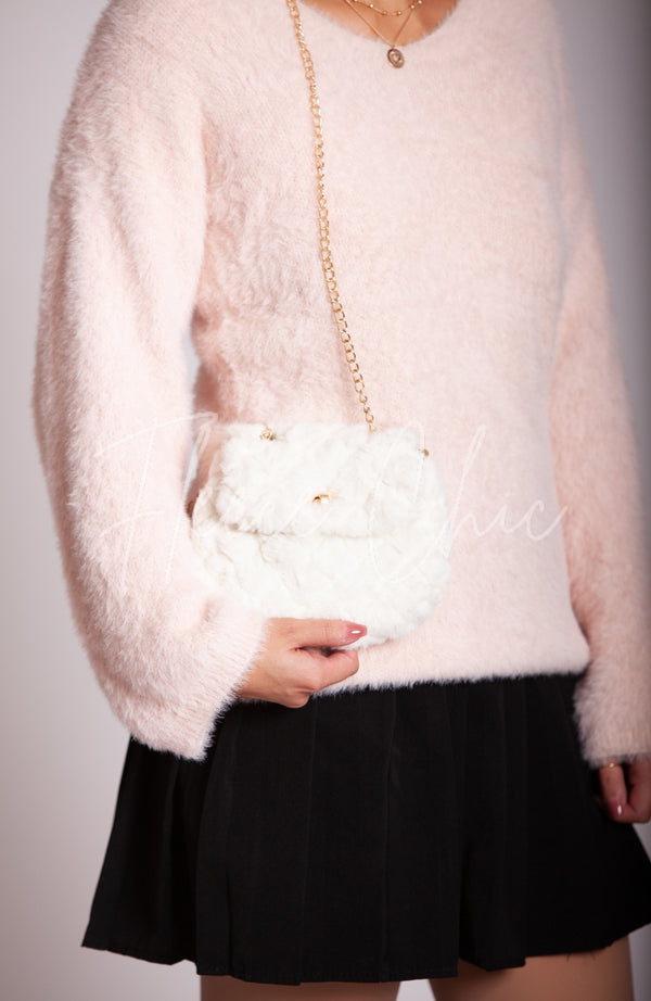 A woman in a pink fuzzy sweater holds a fur purse that is white with a golden chain - Fleece Chic