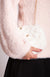 A woman wearing a pink fuzzy sweater holds a white fur purse by Fleece Chic.