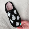 One part of a pair of fuzzy slippers with ghost motifs is held up on display - Fleece Chic