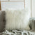 A white Mongolian sheep pillow cover with a hidden zipper, placed on a couch with a grey blanket and a modern chair in the background - Fleece Chic