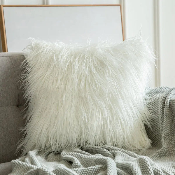 A white Mongolian sheep pillow cover with a hidden zipper, placed on a couch with a grey blanket and a modern chair in the background - Fleece Chic