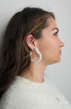 A woman wears a white sweater paired with heart shaped earrings by Fleece Chic.