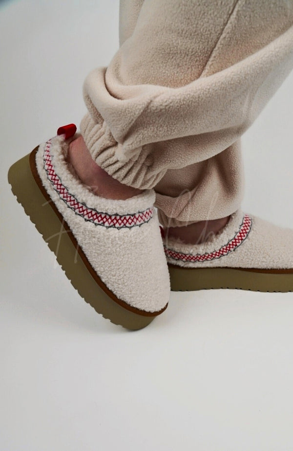 A person wears white Curly Tasman Platform Slippers by Fleece Chic and displays their side profile.