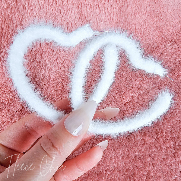 A close-up of heart shaped earrings on a fluffy pink background - Fleece Chic.