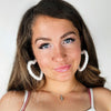 A woman wears heart shaped earrings that are white and fluffy by Fleece Chic.