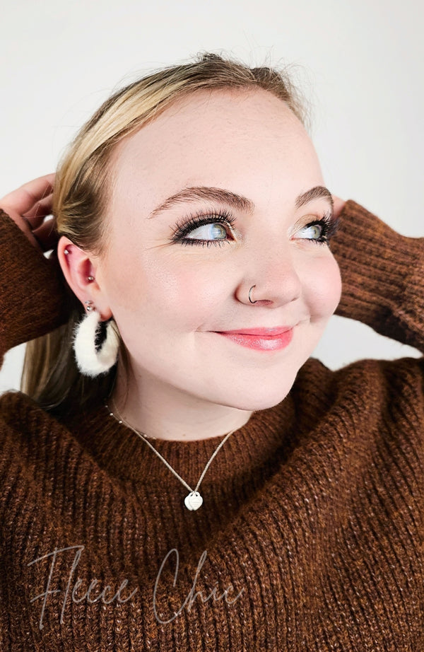 Medium hoop earrings that are white and fluffy are worn by a girl with a brown sweater on - Fleece Chic