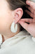 A close-up image of a person's ear wearing medium hoop earrings that are white and fluffy - Fleece Chic