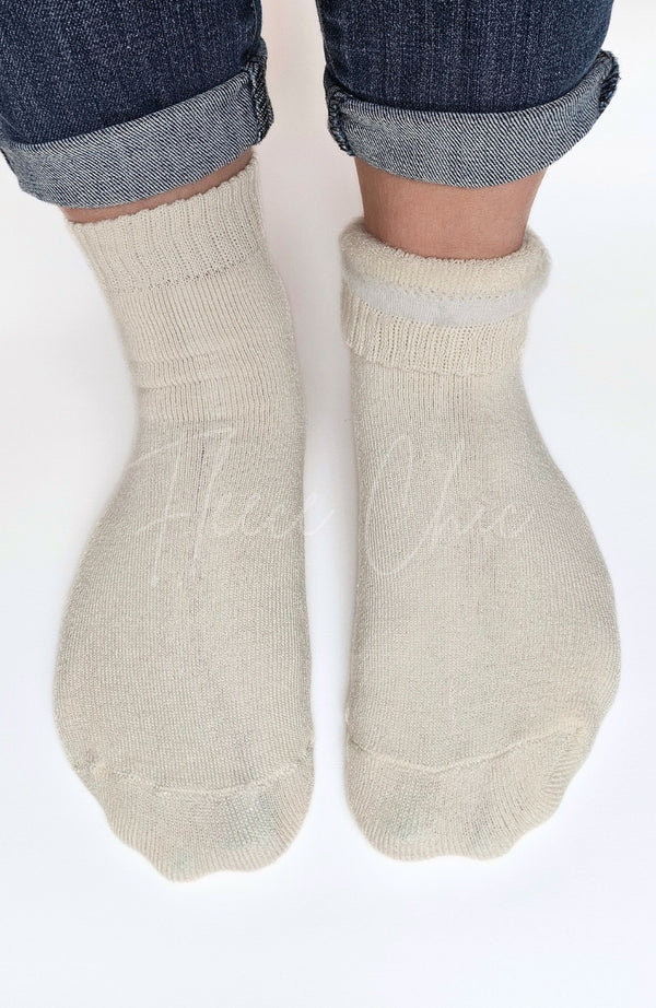 Beige quarter socks with one rolled down partly to show off its plush interior worn with rolled-up jeans on a white background - Fleece Chic