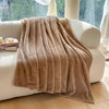 A plush blanket that is khaki is draped over a white fuzzy couch - Fleece Chic