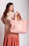 A woman smiling, holding a pink shearling zippered tote bag with shoulder strap by Fleece Chic.