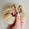 A brown fluffy scrunchie is held up for a detail shot -Fleece Chic