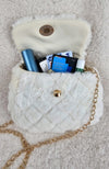 A detailed close-up of a fur purse that is white with diamond patterns on it and golden details has items inside it to show how much it can carry - Fleece Chic