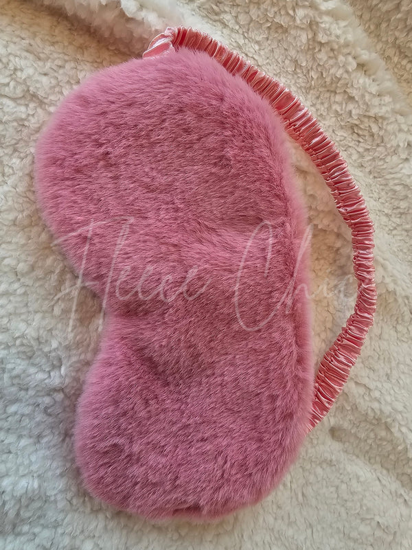 A pink Faux Fur Sleep Mask by Fleece Chic on a beige sherpa background.