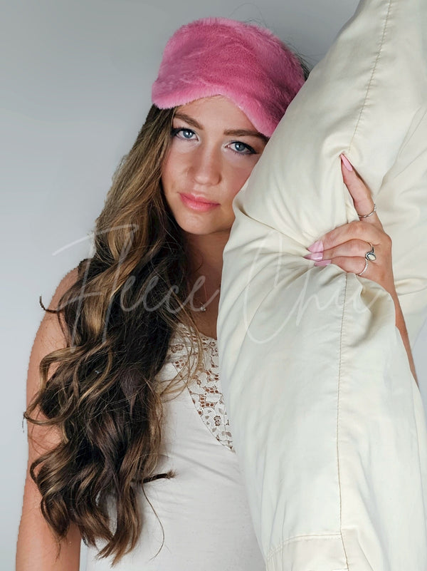 A woman in a nightgown holding a pillow and wearing a pink Faux Fur Sleep Mask by Fleece Chic.