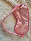 The backside of a pink Faux Fur Sleep Mask by Fleece Chic on a beige sherpa background.