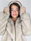 A woman poses holding fur earmuffs over her ears while wearing a fox fur coat by Fleece Chic.